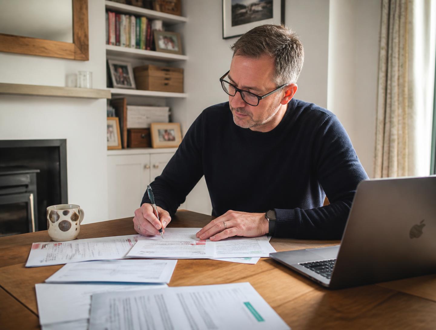 A man working calmly through paperwork and a laptop at his dining table